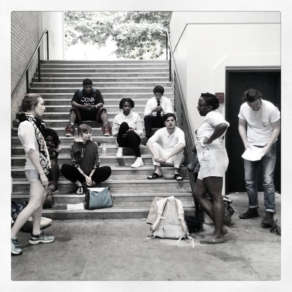 A black and white photo of a group of people of many races, body types, and genders, sitting on a set of steps.