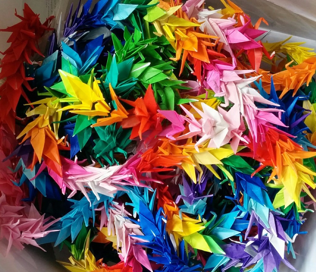 A close-up of dozens of colorful, miniature paper cranes.
